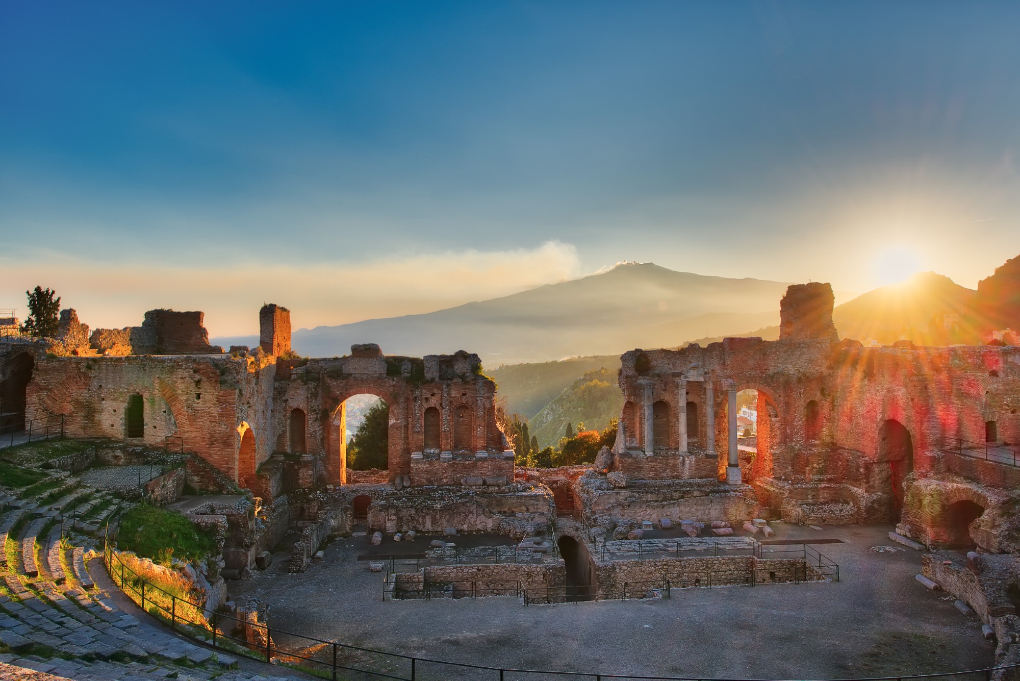 Particular of Ancient theatre of Taormina with Etna erupting vol